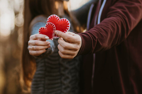 Ein Liebespaar hält zwei rote Herzen in der Hand zum Valentinstag